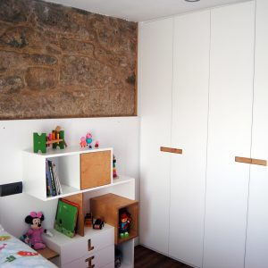 dormitorio infantil de niña con estanterías, mesitas de noche y armario blancos y pared de piedra