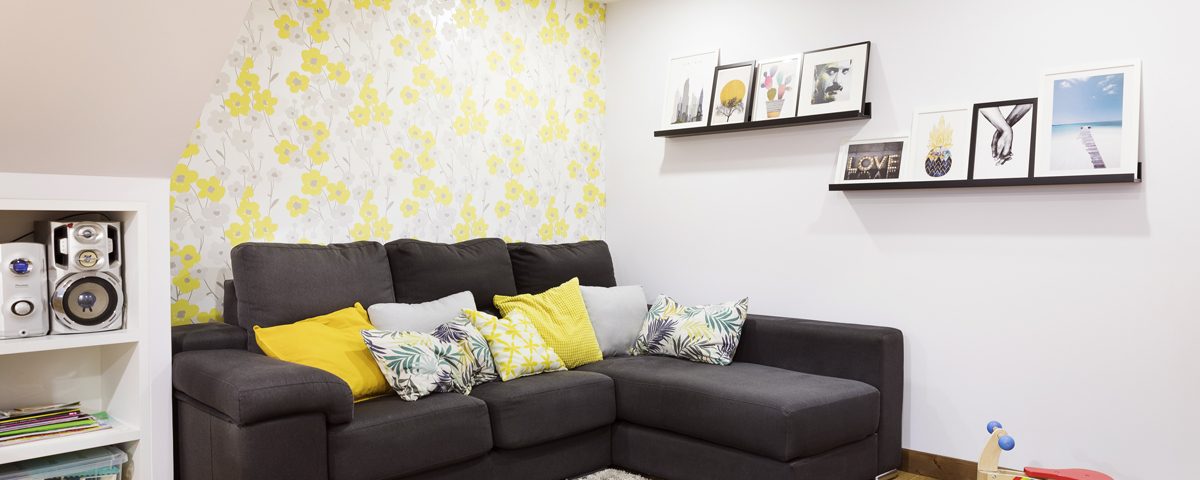 Sofá del salón de Abraite, en color negro con cojines amarillos a juego conlas paredes blancas y amarillas y una estantería negra con cuadros