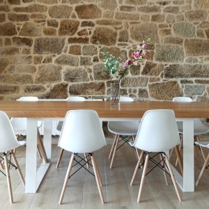 Mesa de comedor en madera con patas blancas y sillas a juego frente a una pared de piedra