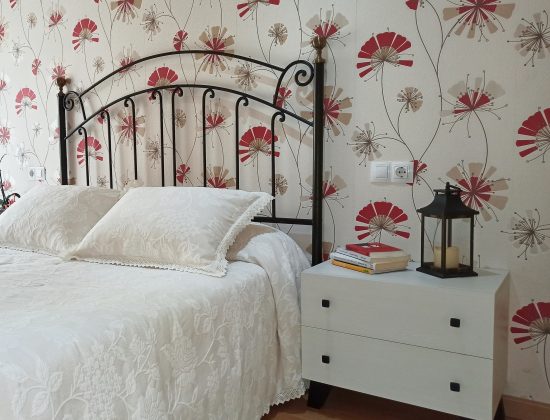 Dormitorio con cabecero de cama de matrimonio negro, cama blanca y mesitas blancas